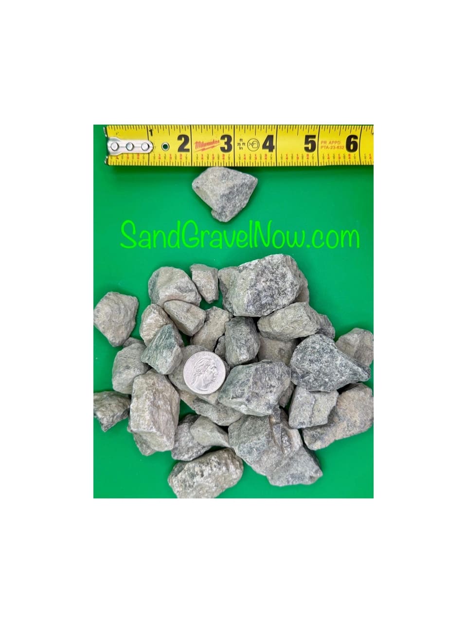 Angular gray 1-1/2 inch crushed rock pieces on a green board with a quarter and a tape measure for scale.