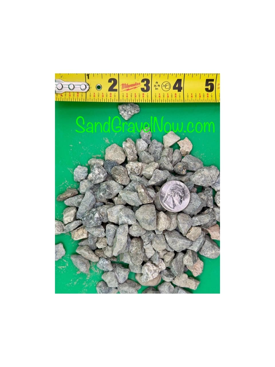 Gray 1/2 inch crushed rock pieces heaped on a green board with a quarter and a tape measure for scale.