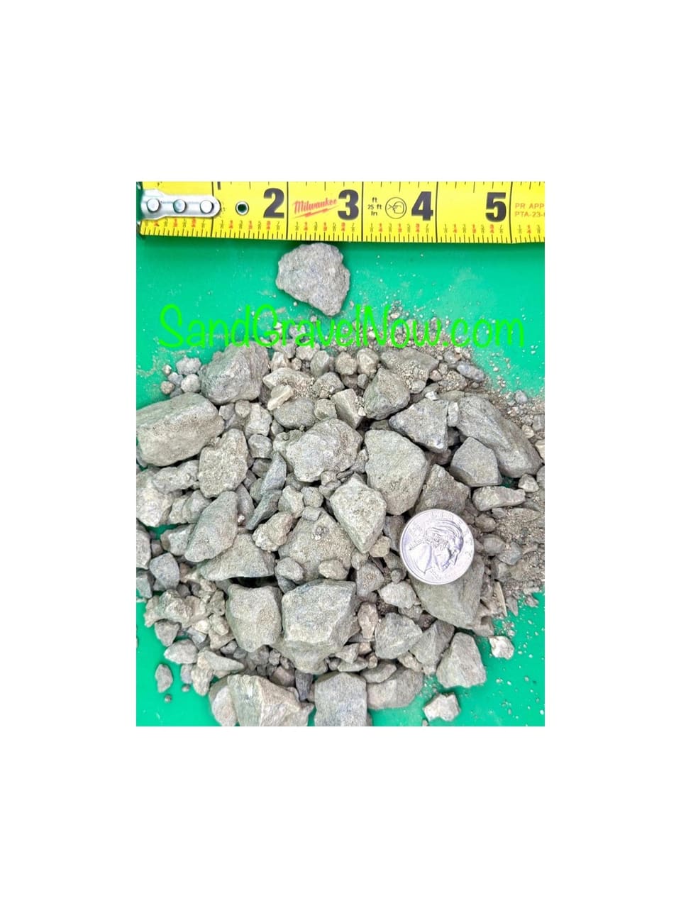 Class 2 road base, gray angular rock with fines, on a green board beside a tape measure and a quarter for scale.