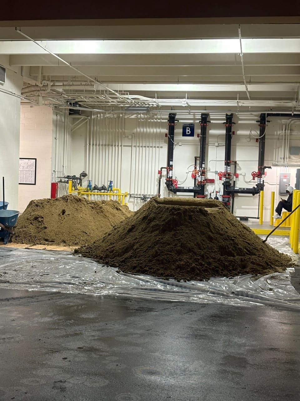 Two piles of tan, fine-grained material on plastic sheeting on a wet concrete floor inside a loading dock area.