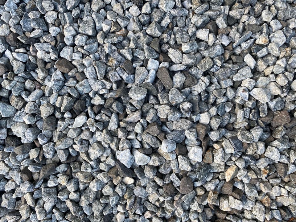 Close-up of loose angular crushed granite in light gray, white and dark gray, pieces roughly half to three-quarters of an inch, filling the frame.