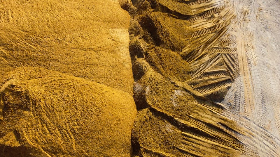 Overhead view of golden-brown sand mounds with tire tracks pressed into the loose material and packed lighter ground to the right.